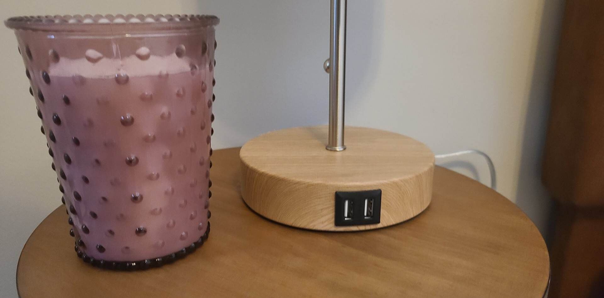 Una mesa redonda de madera con un reloj digital y un vaso rosa con textura.
