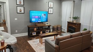 A living room with a flat-screen TV, a brown leather sofa, a wooden coffee table, and a fireplace. - Cozy Home in Heart of Prestonsburg (Prestonsburg)