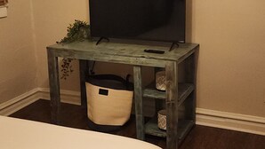A bedroom with a bed, a TV on a wooden stand, a small plant, and a trash bin. - Cozy Home in Heart of Prestonsburg (Prestonsburg)