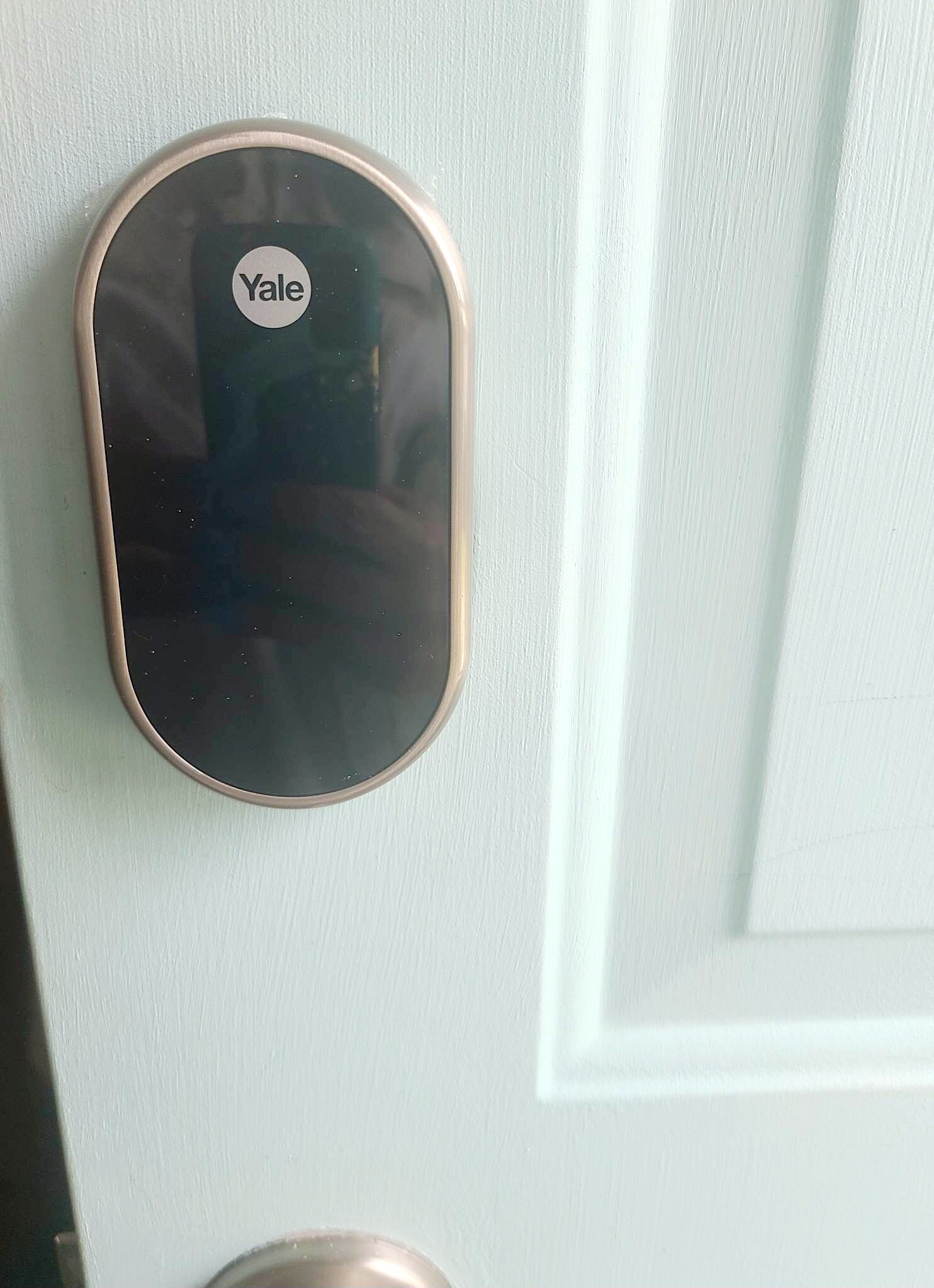 Une serrure intelligente de la marque Yale, montée sur une porte blanche.