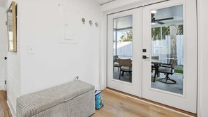 A room with a bench, a sliding glass door leading to an outdoor patio with a table and chairs. - Heated Pool + Putting Green | Walk to Beach (Tybee Island)