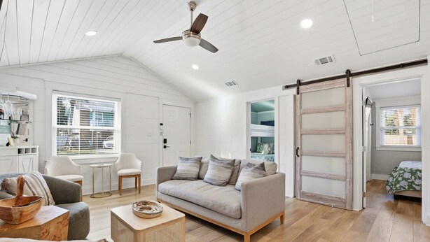 A spacious living room with a grey sofa, wooden coffee table, and a ceiling fan. - Heated Pool + Putting Green | Walk to Beach (Tybee Island)