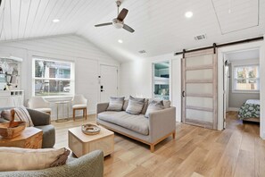 Ein geräumiges Wohnzimmer mit grauem Sofa, Couchtisch aus Holz und Deckenventilator.