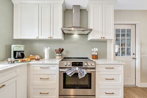 A kitchen with white cabinetry, a stainless steel stove, and a window with a view of the outside.