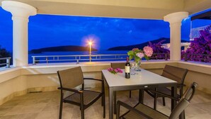 Un espace extérieur aménagé pour les repas, avec une table et des chaises, offrant une vue sur un plan d’eau et des collines au crépuscule.