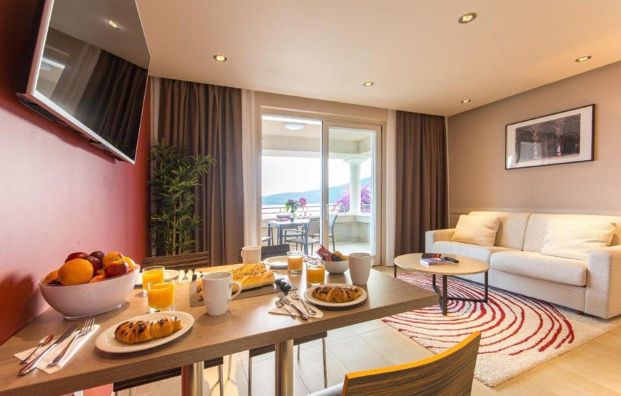 Habitació d'hotel moderna amb zona de menjador, un sofà i un balcó amb vistes.