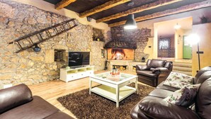 Una sala de estar acogedora con pared de piedra, chimenea, mobiliario de cuero y televisor.