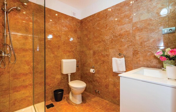 Une salle de bain avec une douche à parois de verre, des toilettes, un lavabo et une poubelle.