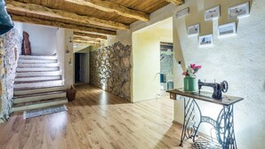 Un interior rústico con vigas de madera, una pared de piedra, una máquina de coser y una escalera.