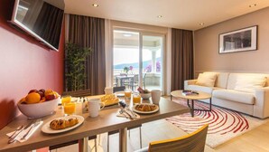 Una habitación de hotel moderna con zona de comedor, sofá y balcón con vistas.