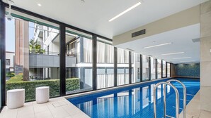 Une piscine intérieure avec des parois en verre transparent, un sol carrelé et des échelles métalliques.