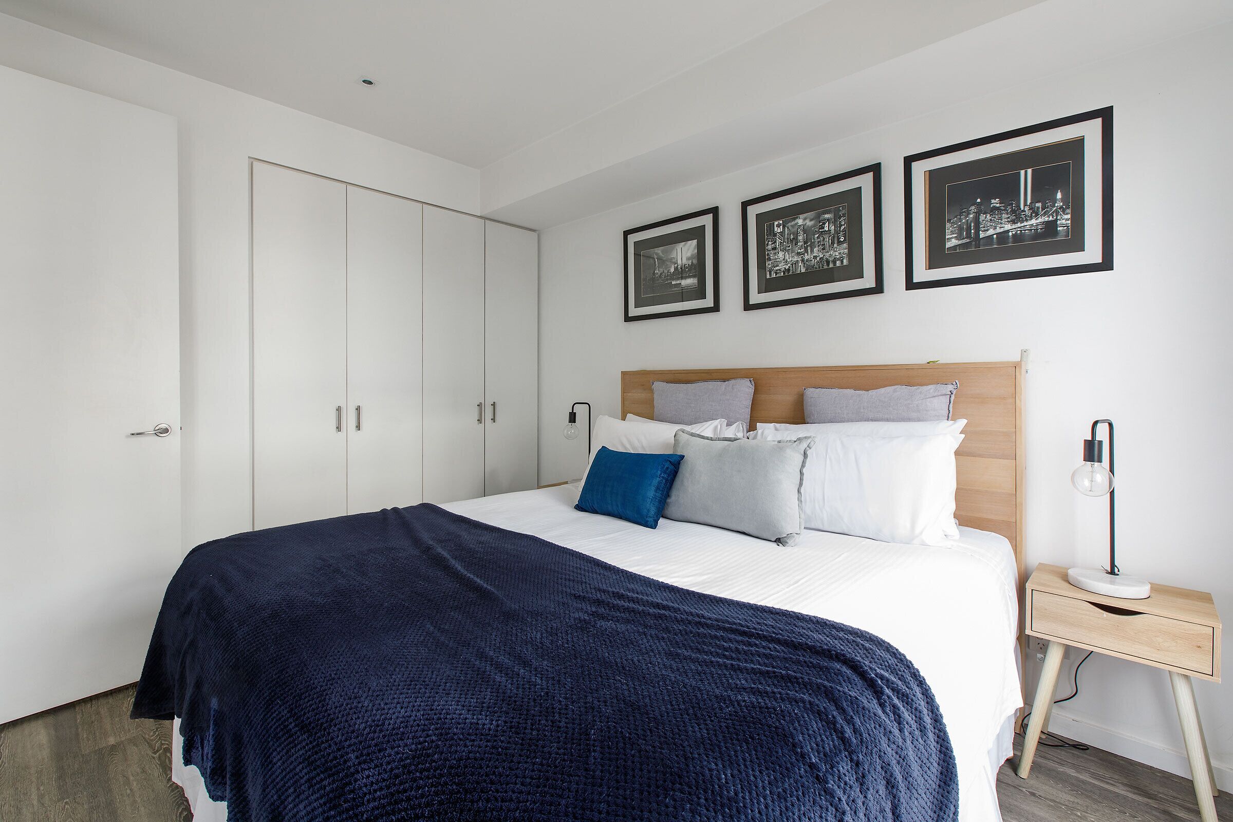 A bedroom with a bed, a bedside table, a lamp, and three framed pictures on the wall.