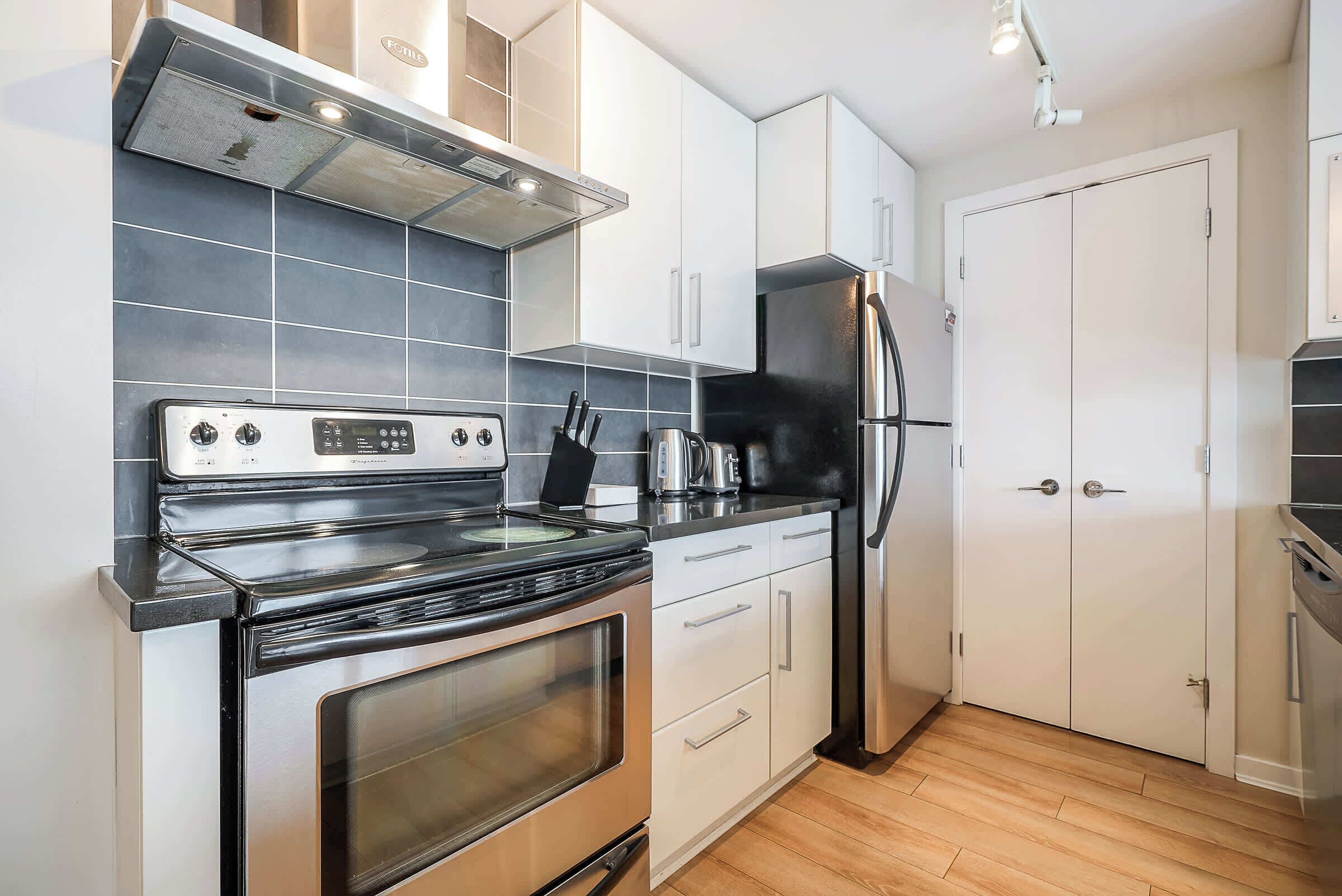 A modern kitchen with a stainless steel stove, white cabinets, and a black refrigerator.