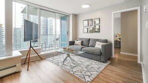 A modern living room with a grey sofa, a glass coffee table, and a large window with a city view.