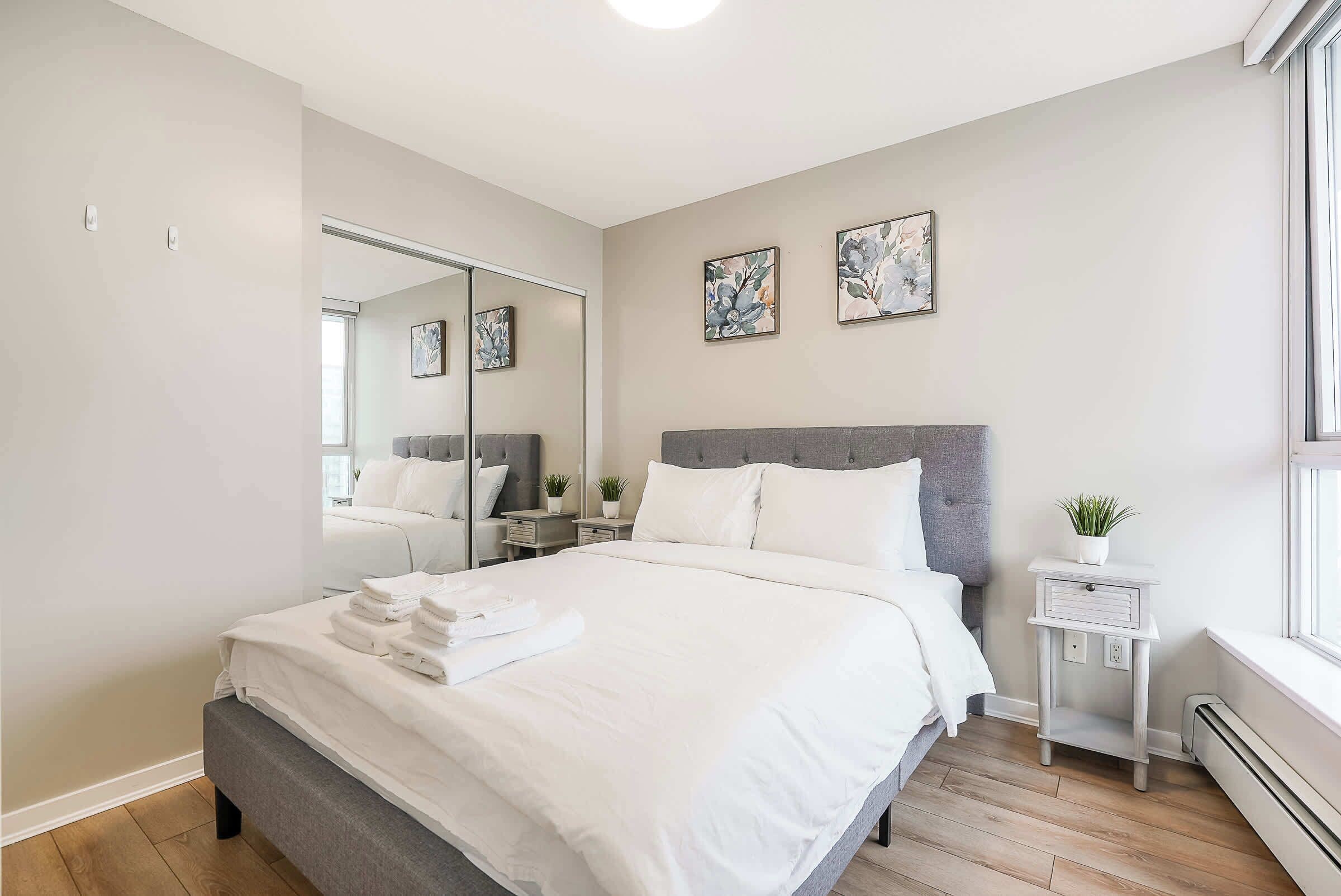 Une chambre à coucher moderne avec un grand lit, une table de chevet avec une lampe, une petite plante et des œuvres d’art accrochées au mur.