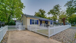A small, single-story building with a white picket fence, a concrete driveway, and a clear sky.