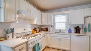 A kitchen with white cabinets, a stove, a microwave, a dishwasher, and a window with blinds.