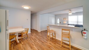 A kitchen with wooden flooring, a white refrigerator, and a dining table with chairs.
