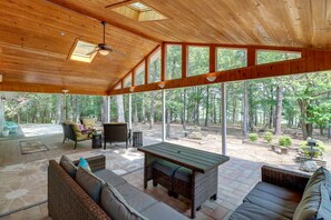 Un espacio de estar abierto con techo de madera, ventanas amplias y vistas al exterior de un bosque.