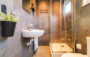 Ein modernes Badezimmer mit einem weißen Waschbecken, einer Duschkabine aus Glas und einer Toilette.