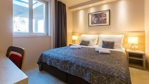Hotellihuone, jossa on sänky, työpöytä, tuoli, ikkuna ja taulu seinällä.