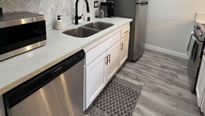 A modern kitchen with white cabinets, stainless steel appliances, a double sink, and a patterned rug. - Minutes from Carlsbad Downtown and Beach (Carlsbad)
