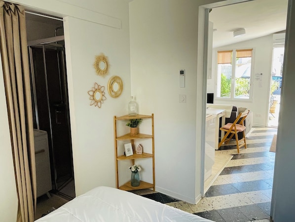 A hotel room with a bed, a wooden shelf with decorative items, a mirror, and a view of the outdoor area.