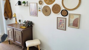 Un mur orné de différents types de nattes tissées, un tableau encadré, une petite plante en pot, une lampe et un banc.