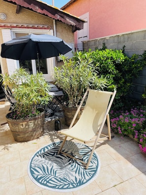 A patio with a chair, potted plants, and an umbrella.