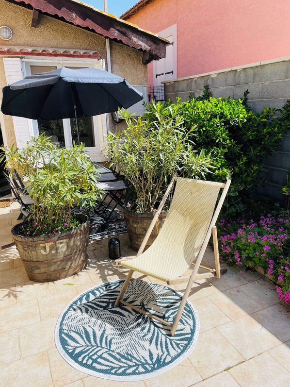 Une terrasse avec une chaise, des plantes en pot et un parasol.