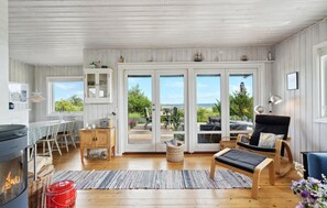 A spacious living room with a fireplace, wooden flooring, a dining area, and large sliding glass doors leading to a deck with a view of the outdoors. - Beautiful home in Faaborg with kitchen (Faaborg)