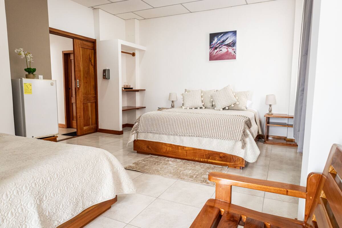 Een hotelkamer met twee bedden, een houten bankje, een tafeltje, een nachtkastje en een schilderij aan de muur.