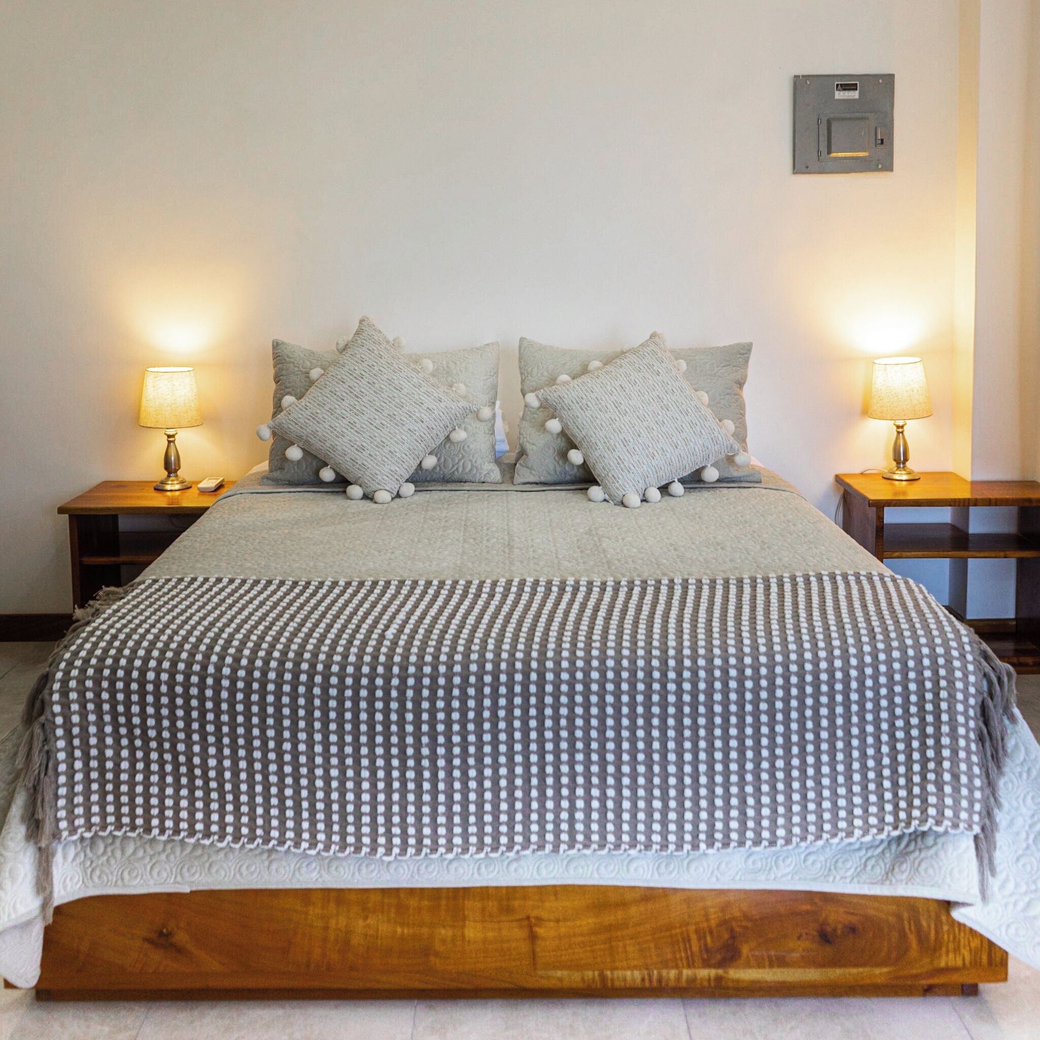 A bed with a grey polka dot bedspread, two matching pillows, and two bedside lamps on wooden nightstands.