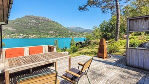 Una terraza de madera con una mesa y sillas, con vista a un lago y montañas.