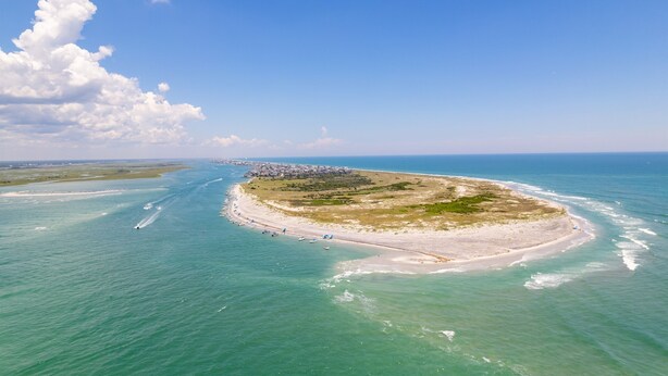 Luchtbeeld van een kustgebied met een zandstrand, een klein eiland en een helderblauwe lucht.