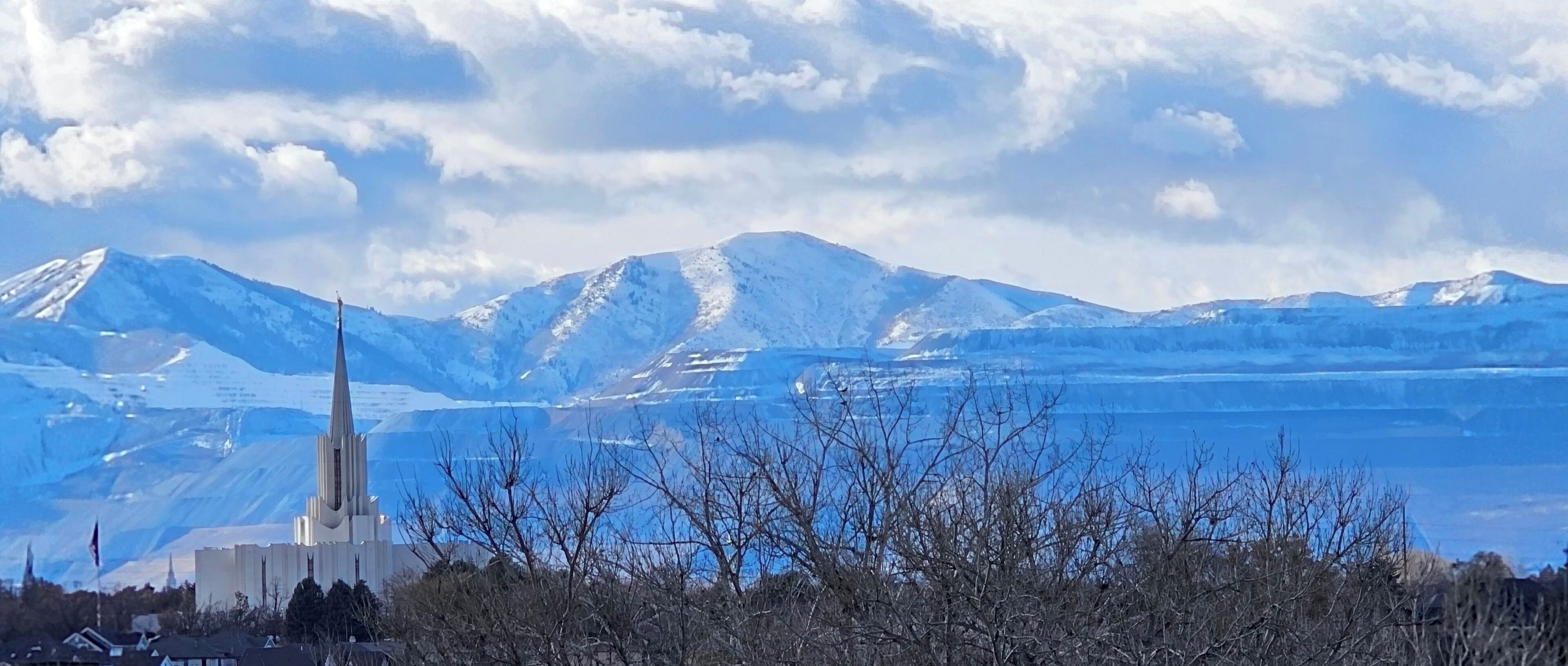 Una iglesia con una aguja alta, rodeada de montañas nevadas y un cielo despejado.