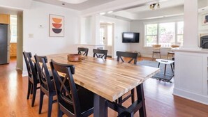 A spacious dining area with a wooden table and chairs, a television mounted on the wall, and a kitchen area visible in the background. - Spacious retreat with outdoor dining, patios and views (Seattle)