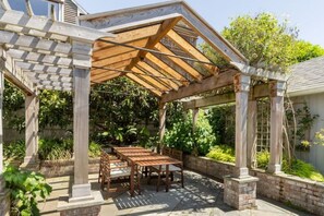 A covered patio area with a wooden table and chairs, surrounded by brick walls and greenery. - Spacious retreat with outdoor dining, patios and views (Seattle)
