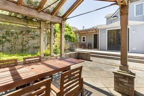 A covered patio with a wooden table and chairs, a stone bench, and a brick fireplace. - Spacious retreat with outdoor dining, patios and views (Seattle)