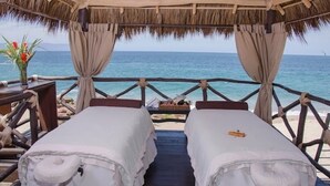 A beachside room with two beds, a thatched roof, and a view of the ocean.