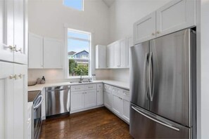 A modern kitchen with white cabinets, stainless steel appliances, and a wooden floor.