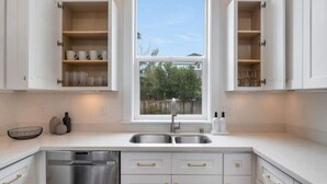 Une cuisine moderne avec des meubles blancs, un lave-vaisselle en acier inoxydable et une fenêtre donnant sur les arbres.