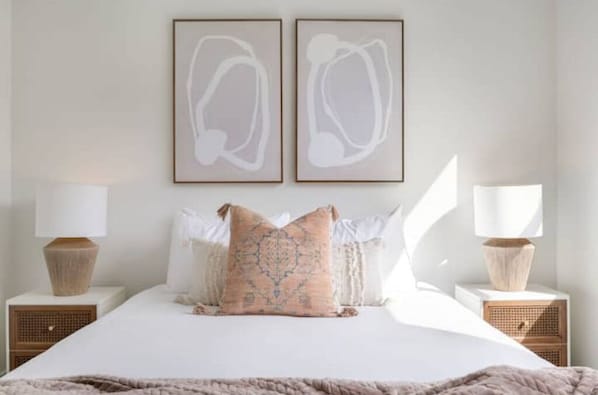 A bedroom with a large bed, two bedside tables with lamps, and abstract wall art.