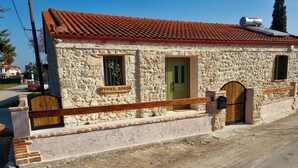 Une maison en pierre avec un toit recouvert de tuiles rouges, une porte verte et une enseigne sur laquelle on peut lire « MAISON EN PIERRE ».