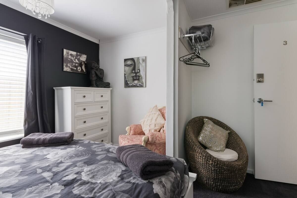 Un dormitorio con cama, cómoda, silla y una obra de arte en la pared.