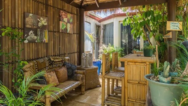 A bamboo-walled room with a cushioned bench, a small table, and potted plants. - Bali in the Barossa (Gawler West)