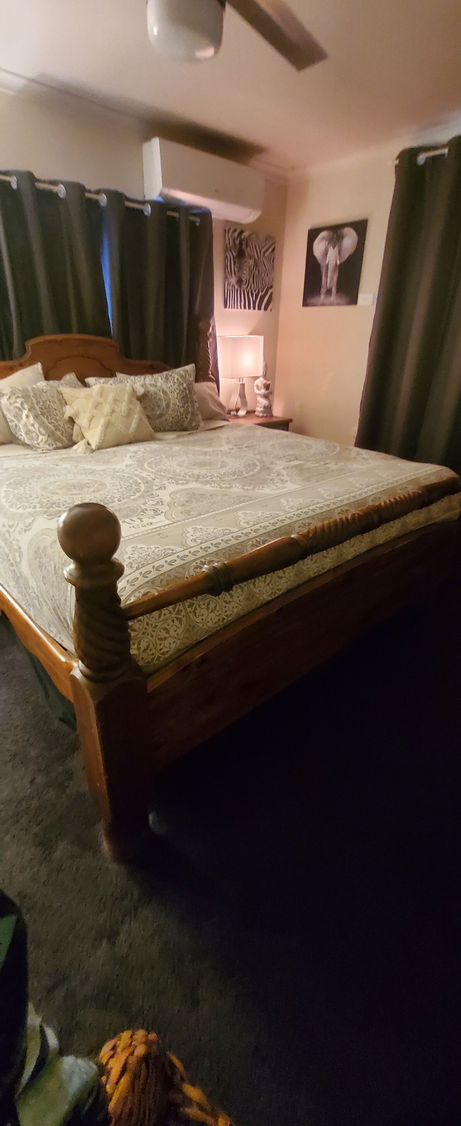 Ein Schlafzimmer mit einem hölzernen Bett, einem Deckenventilator, einem Nachttisch mit Lampe und einem Wandbild mit Zebra-Motiv.