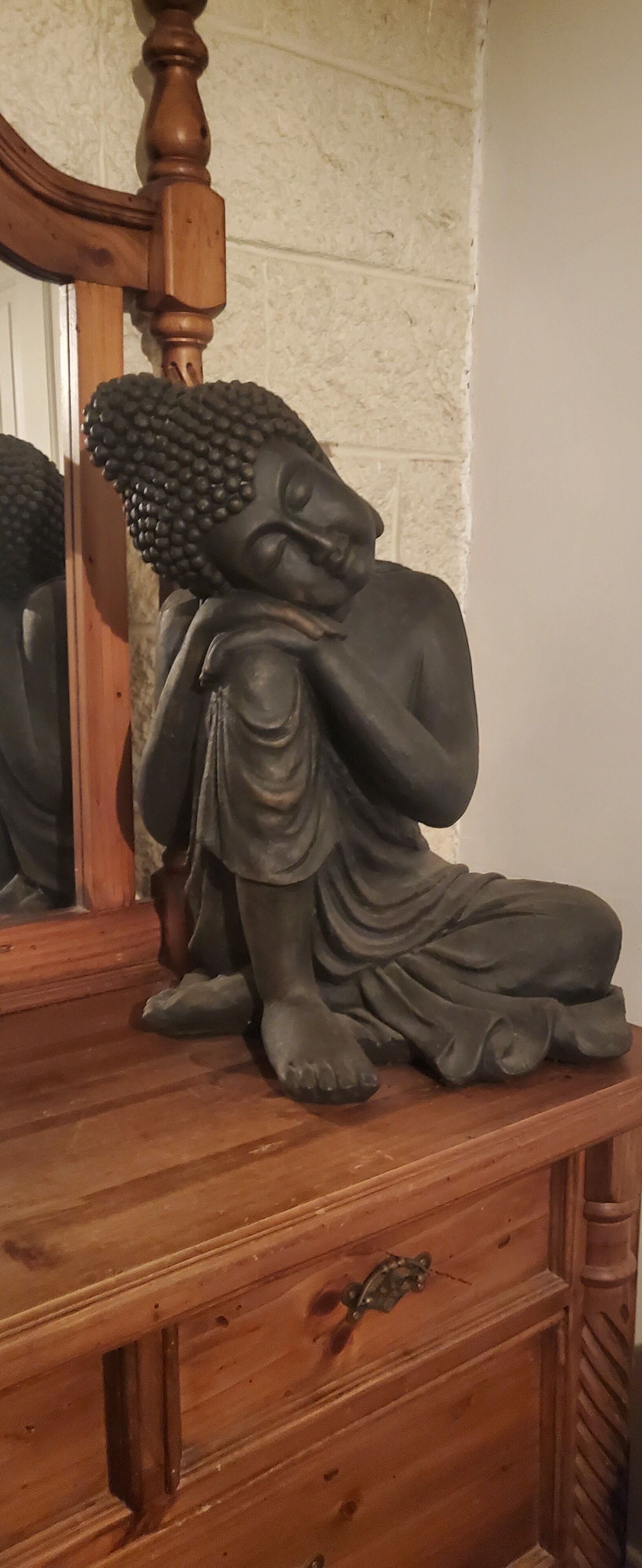 A wooden dresser with a statue of a seated figure.