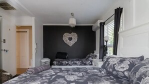 A bedroom with a large bed, a smaller bed, a heart-shaped wall decoration, and a window with curtains. - Bali in the Barossa (Gawler West)