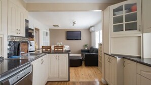 A modern kitchen with a dishwasher, a dining area with a table and chairs, and a living area with a sofa and TV. - Bali in the Barossa (Gawler West)